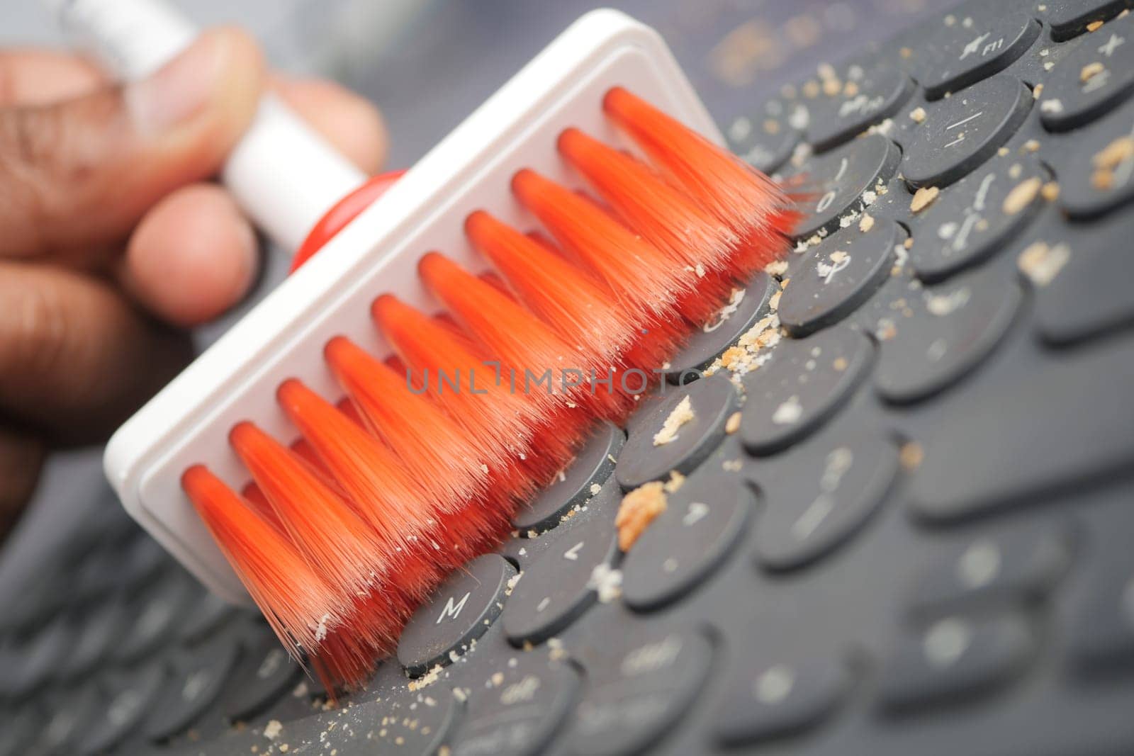 A hand skillfully uses a brush to clean dust and debris from a computer keyboard