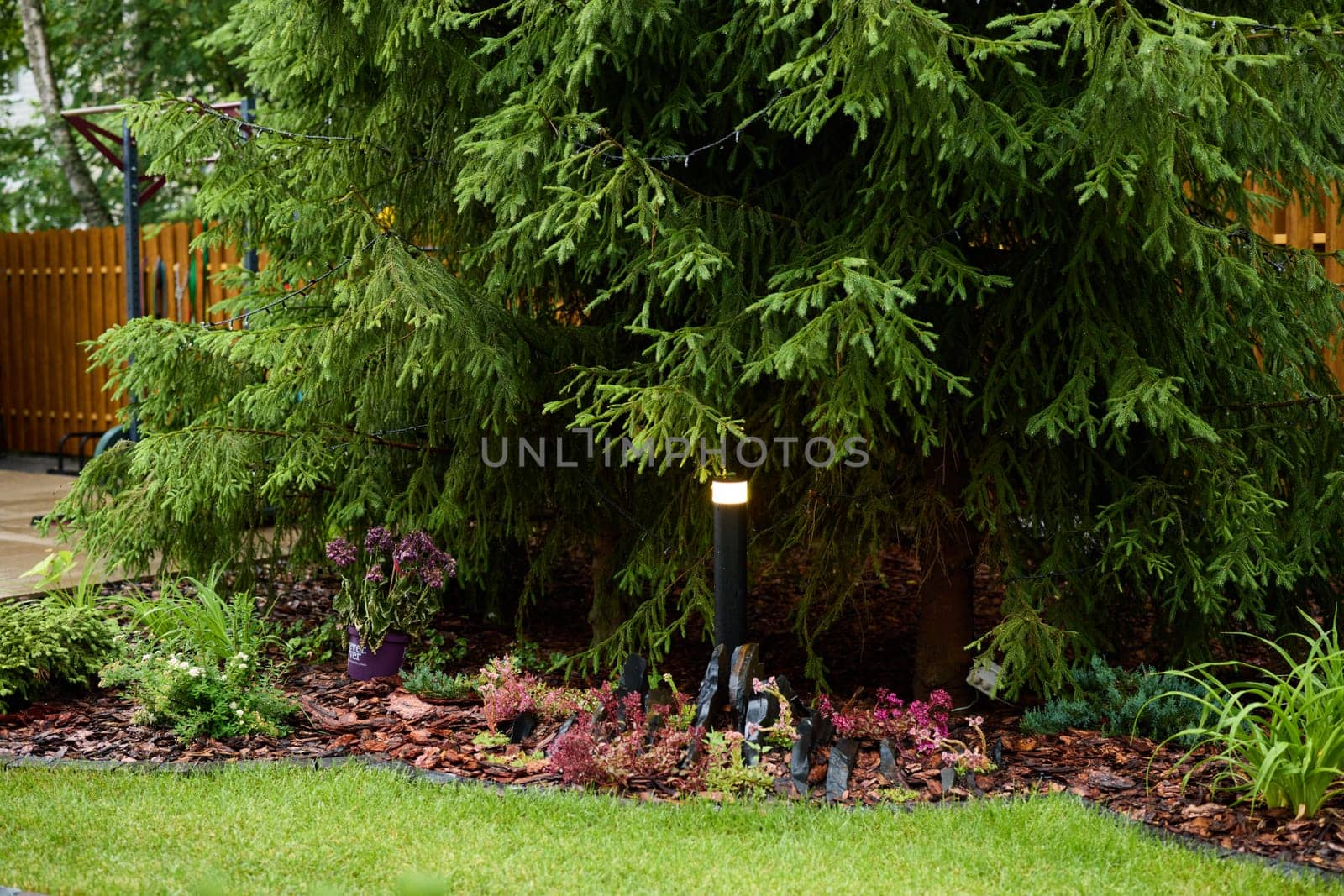 A tranquil garden scene showcasing an array of vibrant plants along with gently glowing LED lighting under a lush tree