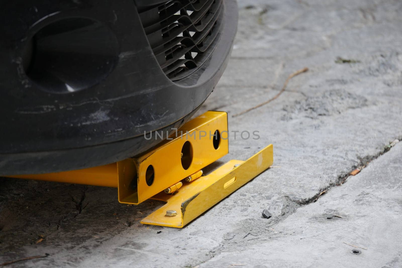 Close-Up of Car Wheel Secured with Yellow Wheel Clamp on Pavement.
