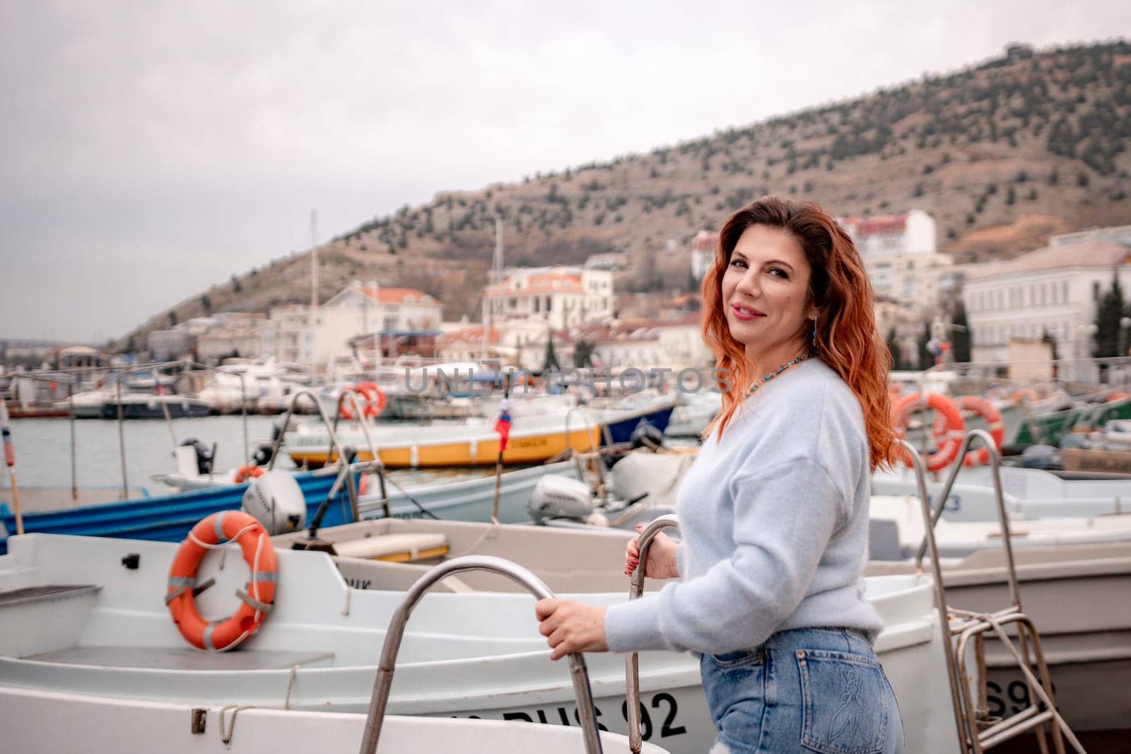 A woman stands in front of a row of boats, some of which have orange life preservers on them. The scene is peaceful and serene, with the boats and the woman creating a sense of calmness and relaxation