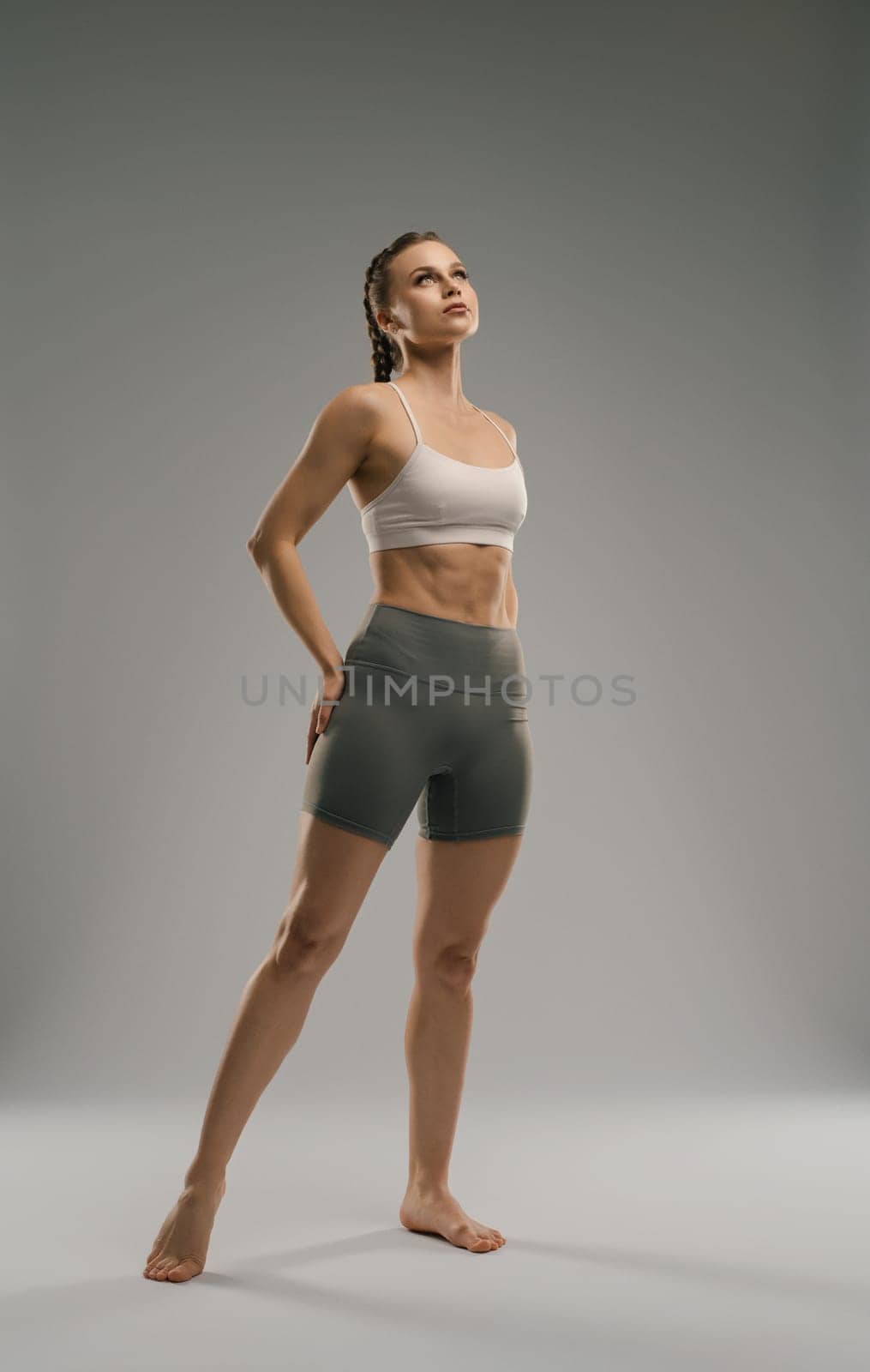 A fitness model stands confidently in a studio, showcasing her toned physique and athletic wear. The soft lighting accentuates her strength and posture, creating an inspiring atmosphere.