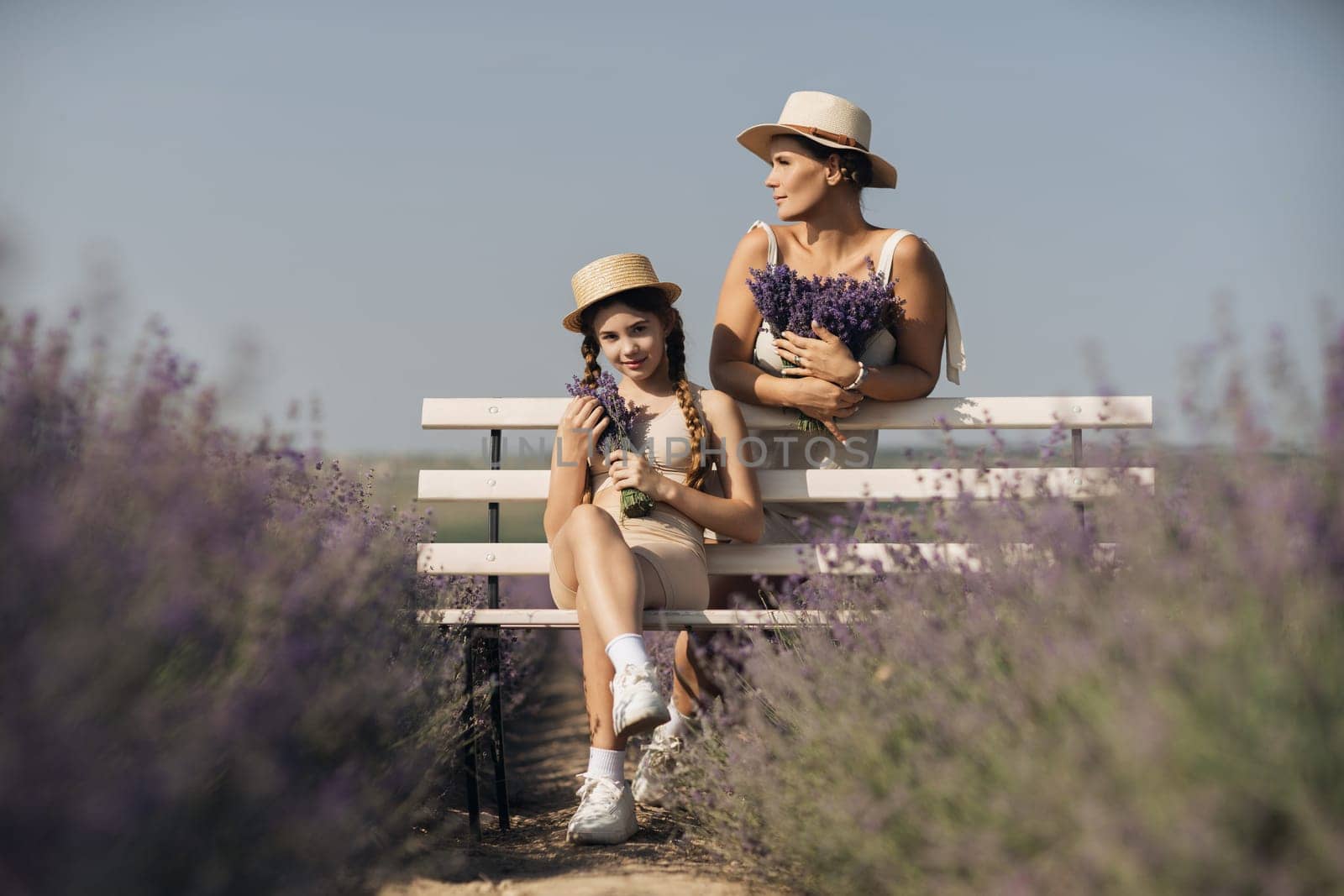 woman child sitting bench in field lavender. The woman is holding a bouquet of flowers, and the child is holding a bouquet as well. The scene is peaceful and serene
