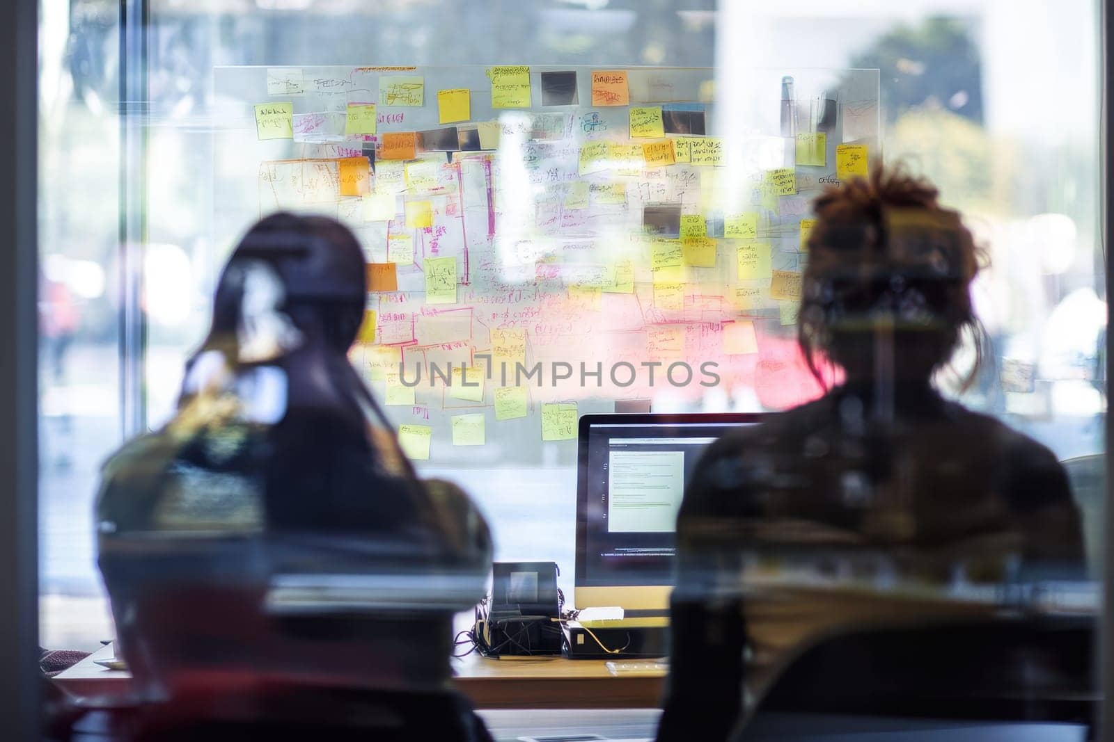 A team in a modern office setting collaborates as they face a wall of colorful notes, showcasing teamwork and creativity.