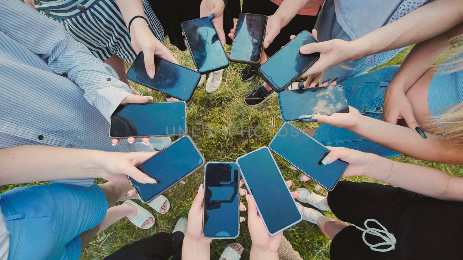 Group of young people standing in a circle on the grass showing their smartphone screens