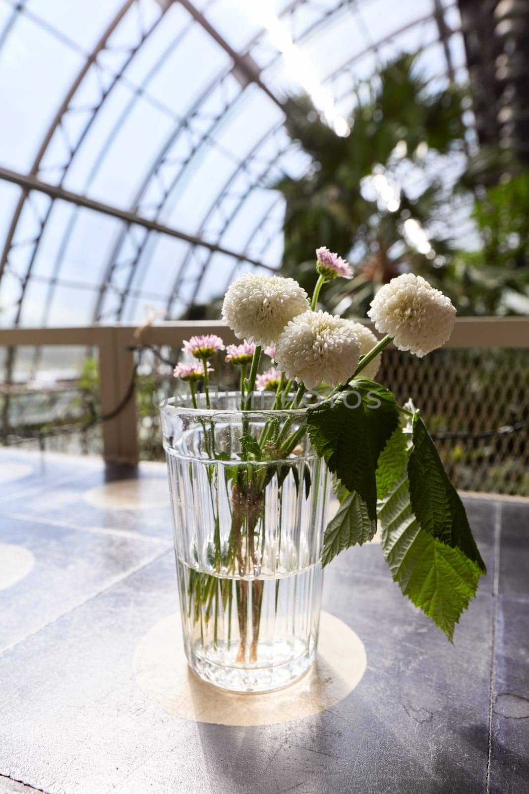 A charming glass vase filled with an abundance of soft white flowers and vibrant, lush greenery all around