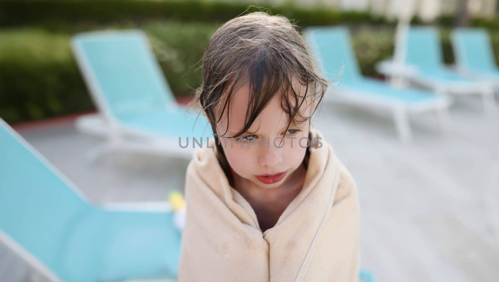 Wet frozen child by the pool, covered with a towel, close-up, blurry. Hypothermia from swimming, summer children's vacation