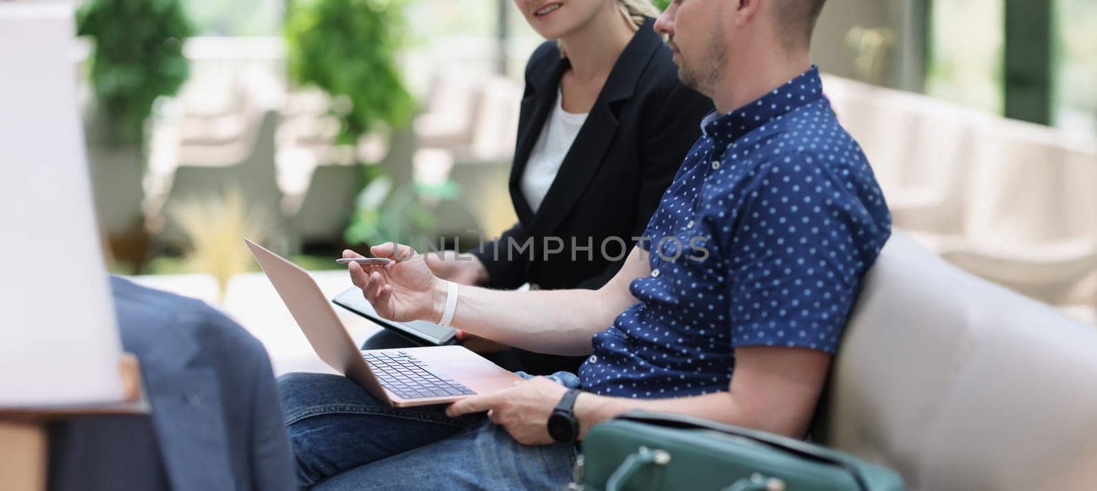 A man with a laptop and a woman with a tablet are talking, close-up, blurry. Negotiating on the street, discussing strategy