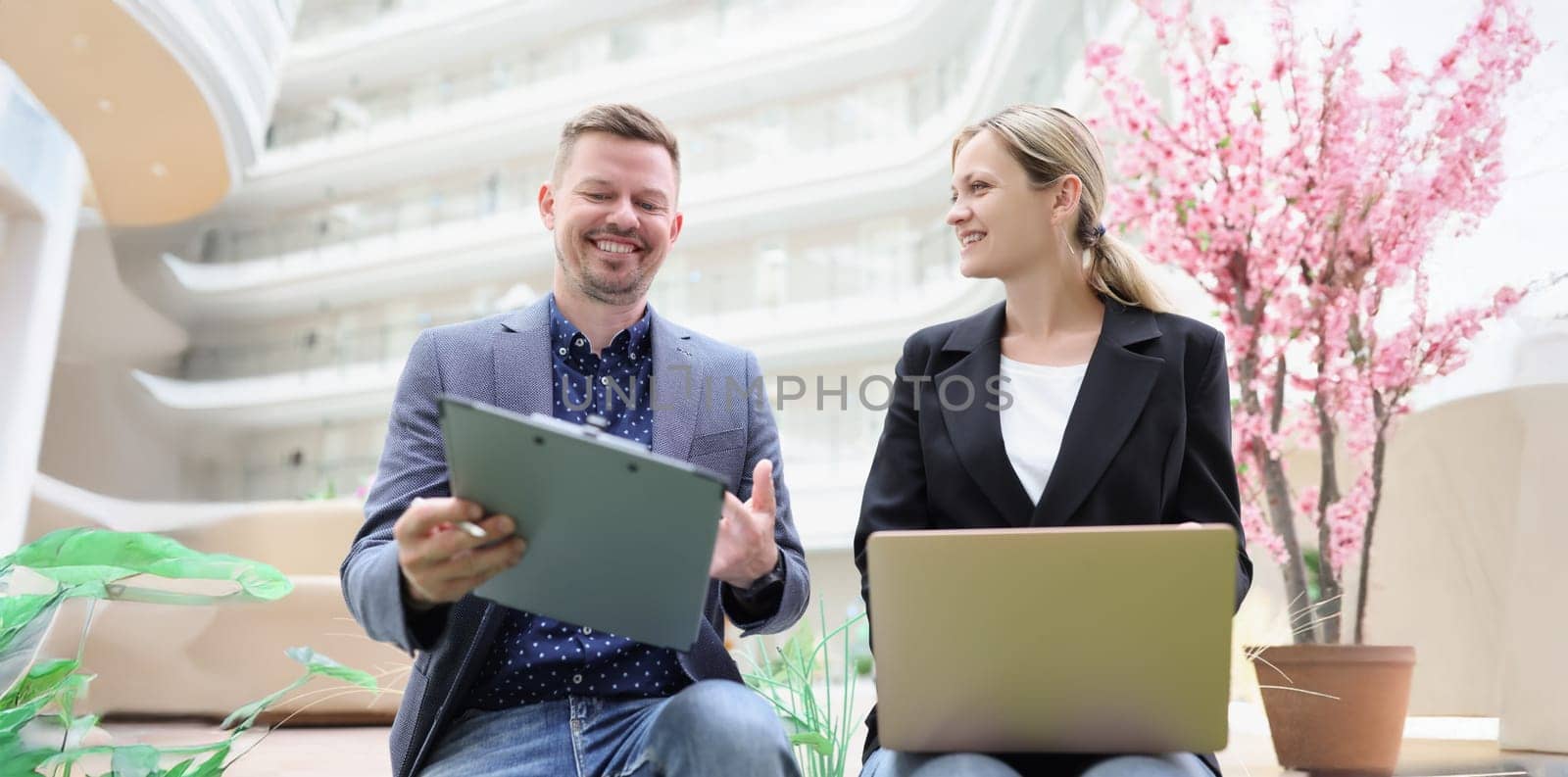 Happy man and woman with laptop and documents are sitting in the lobby of the business center, close-up. The joy of working together