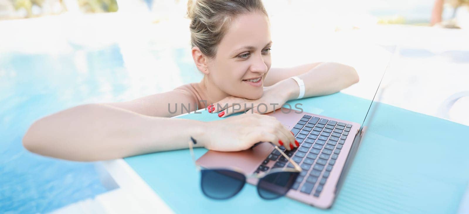 Young woman in the pool uses a laptop, close-up. Freelancer on vacation, luxury resort. Remote work, tourism