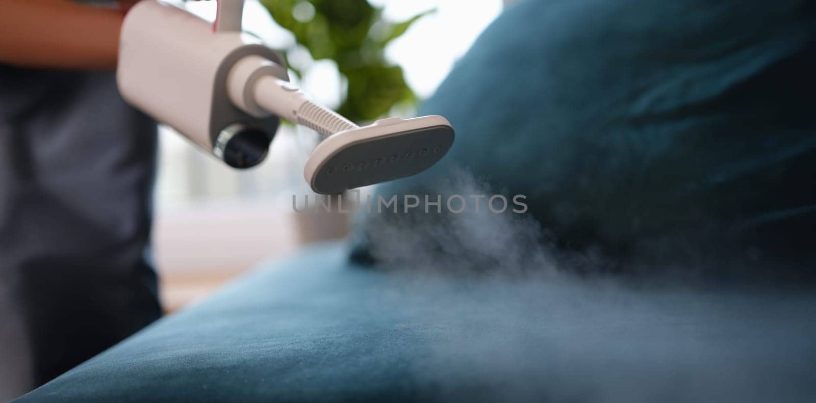Steam comes out of the washing vacuum cleaner above the sofa, close-up, blurry. Hygienic reading of upholstered furniture