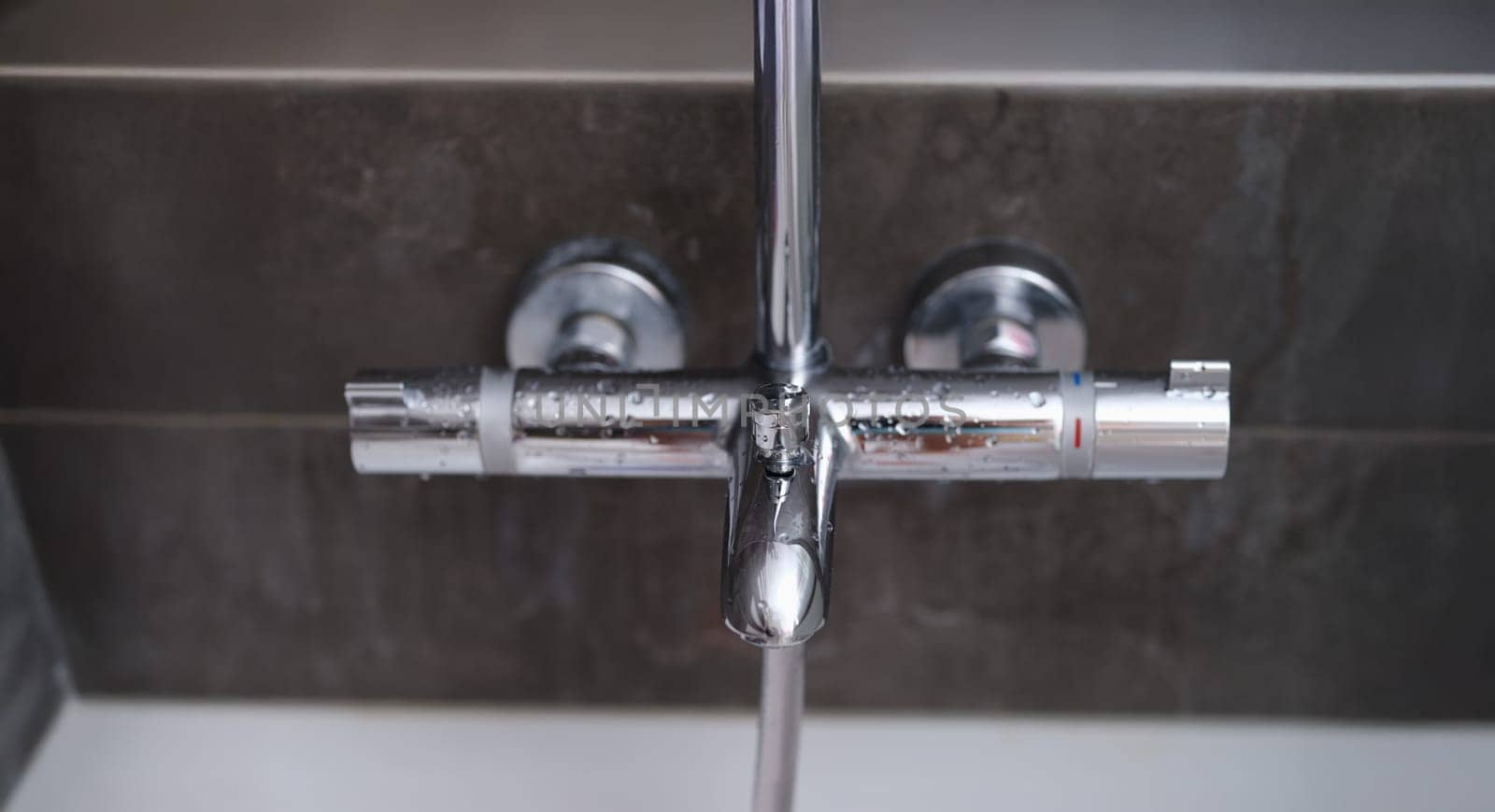 Water drops on the wall mixer in the bathroom, close-up. Chrome faucet on gray background. Plumbing
