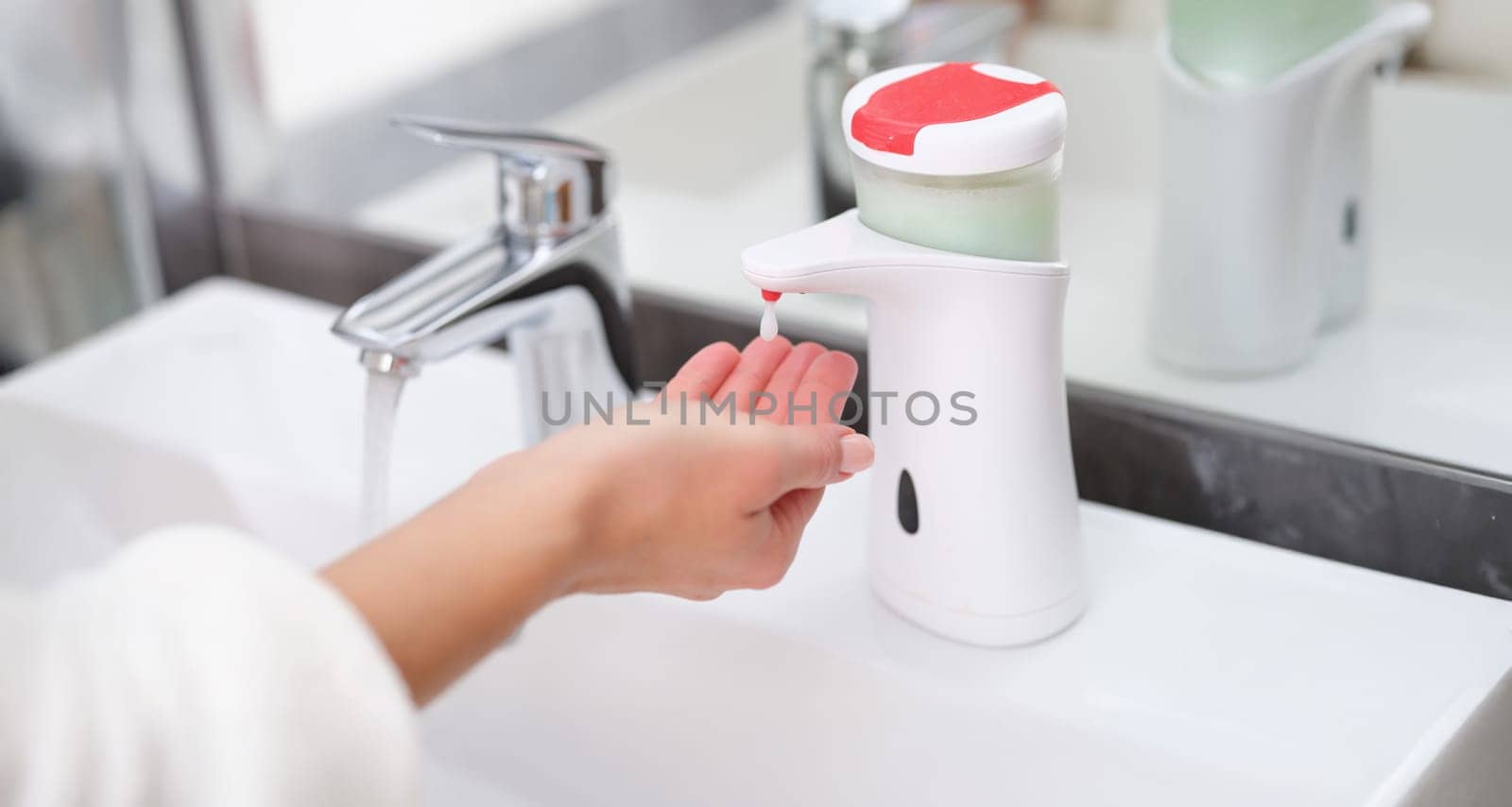 A drop of soap from a dispenser drips onto a woman's hand, close-up. Hand hygiene, bathroom. Washing