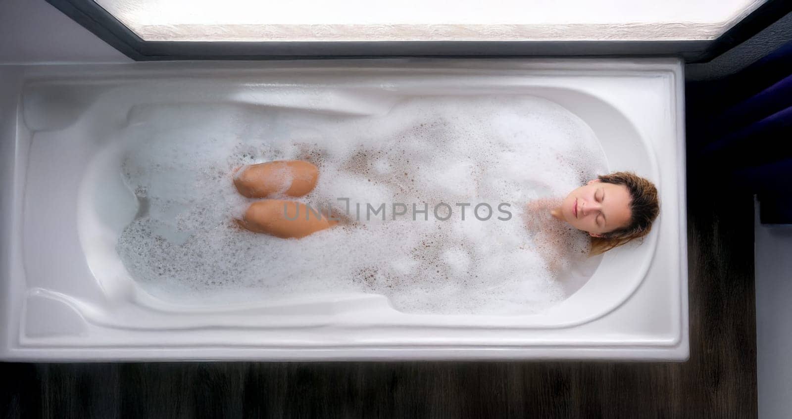 A woman lies in a soapy bath, top view. Relaxation, stress relief, body hygiene, aromatherapy. Beauty treatments, spa