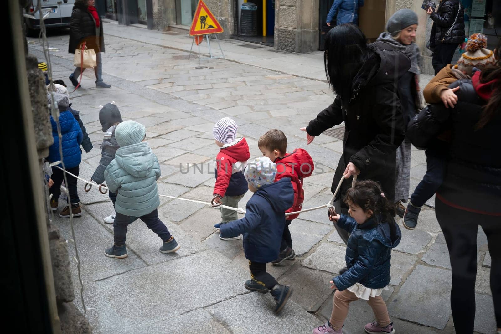 Cremona, Italy - November 20th 2024 Group of kindergarten children walking in line holding a rope with their teachers in cremona, italy