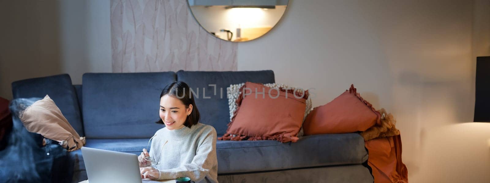 Vertical shot of asian girl sits on floor at home, working on laptop, studying at cozy place, using computer to freelance.