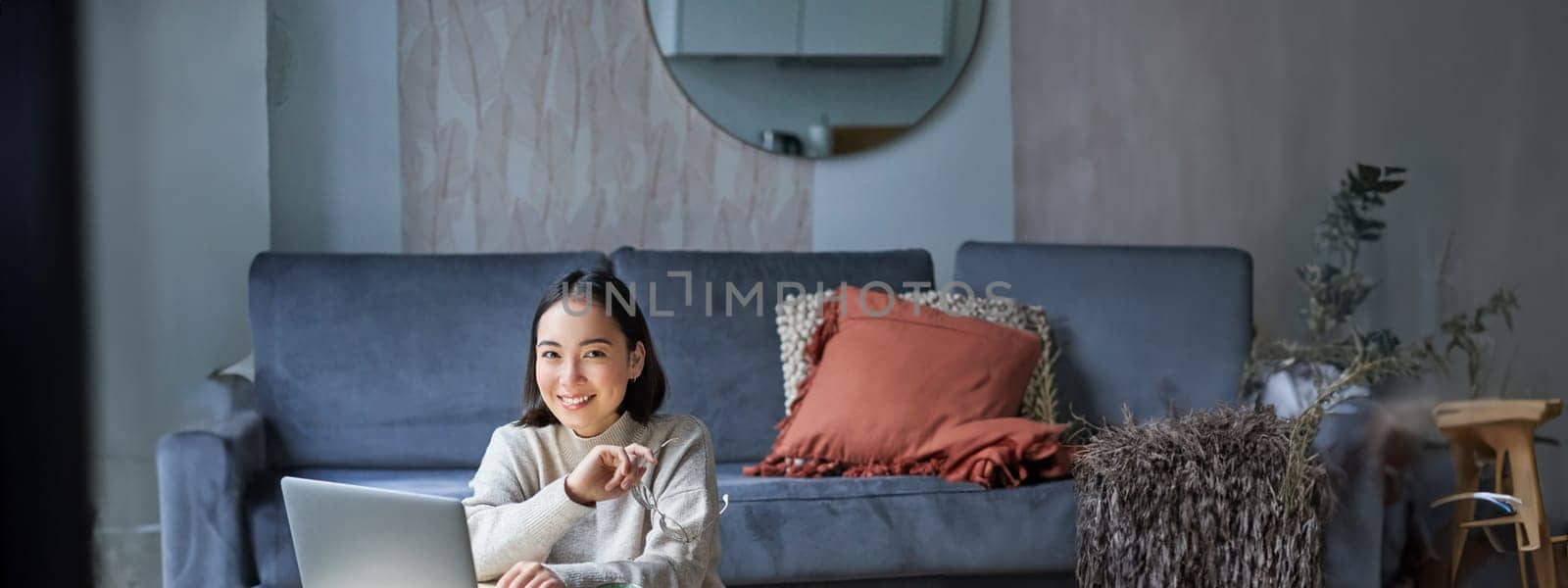 Vertical shot of asian girl sits on floor at home, working on laptop, studying at cozy place, using computer to freelance.