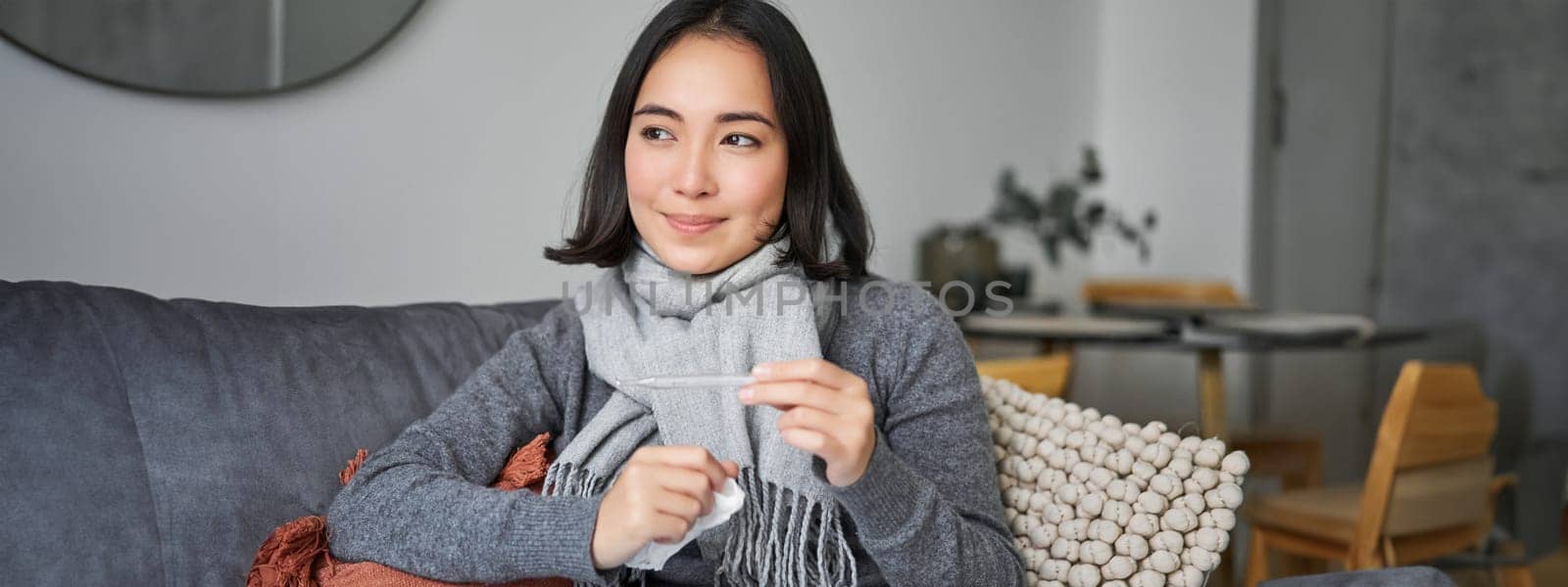 Smiling asian woman holding thermometer and looking pleased, feeling better after cold, got rid of fever, has normal temperature by Benzoix