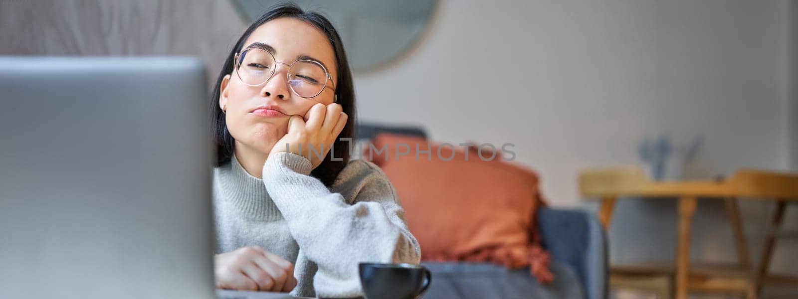 Portrait of korean girl sits bored, student looks gloomy at laptop, sitting at home and expressing boredom.