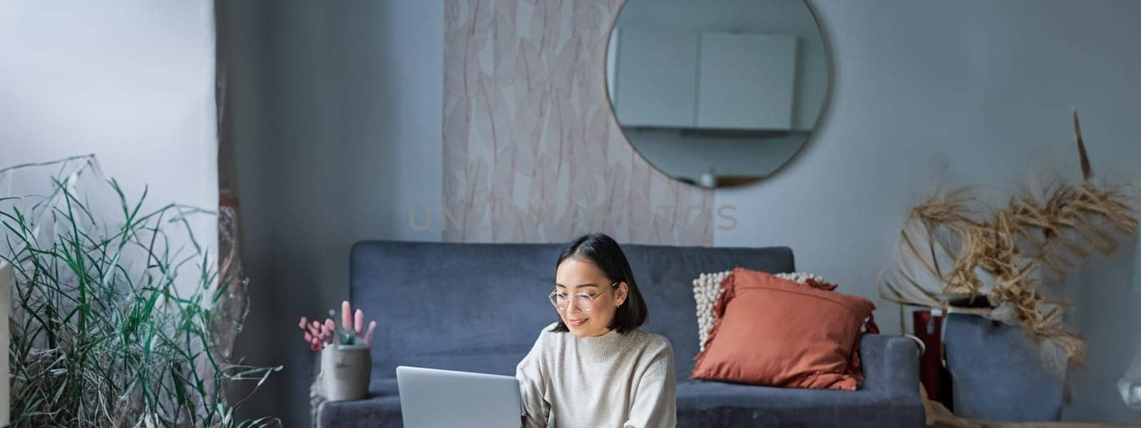 Vertical shot of korean working woman, sitting on floor at home with laptop, studying, using computer on remote, e-learning concept by Benzoix