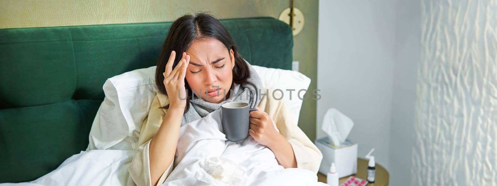 Flu, sickness and people. Young woman feeling sick, having fever and catching col, lying in bed with hot tea, taking drugs from influenza by Benzoix