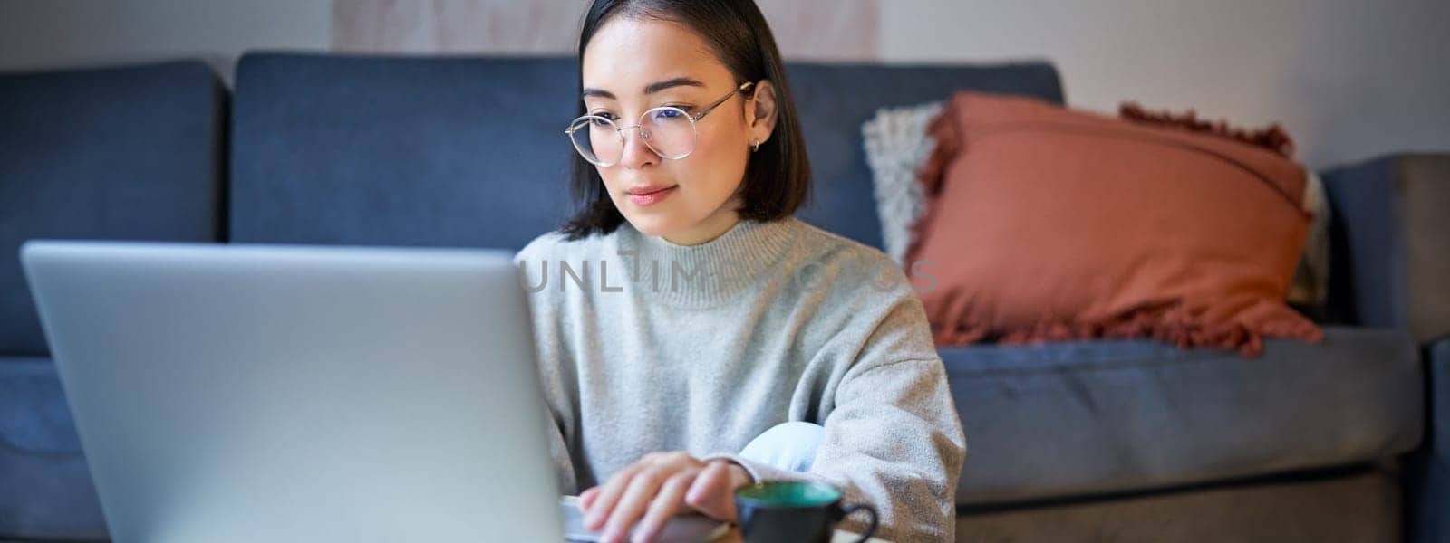 Self employed young korean woman working on remote, typing on laptop, studying at home in living room.