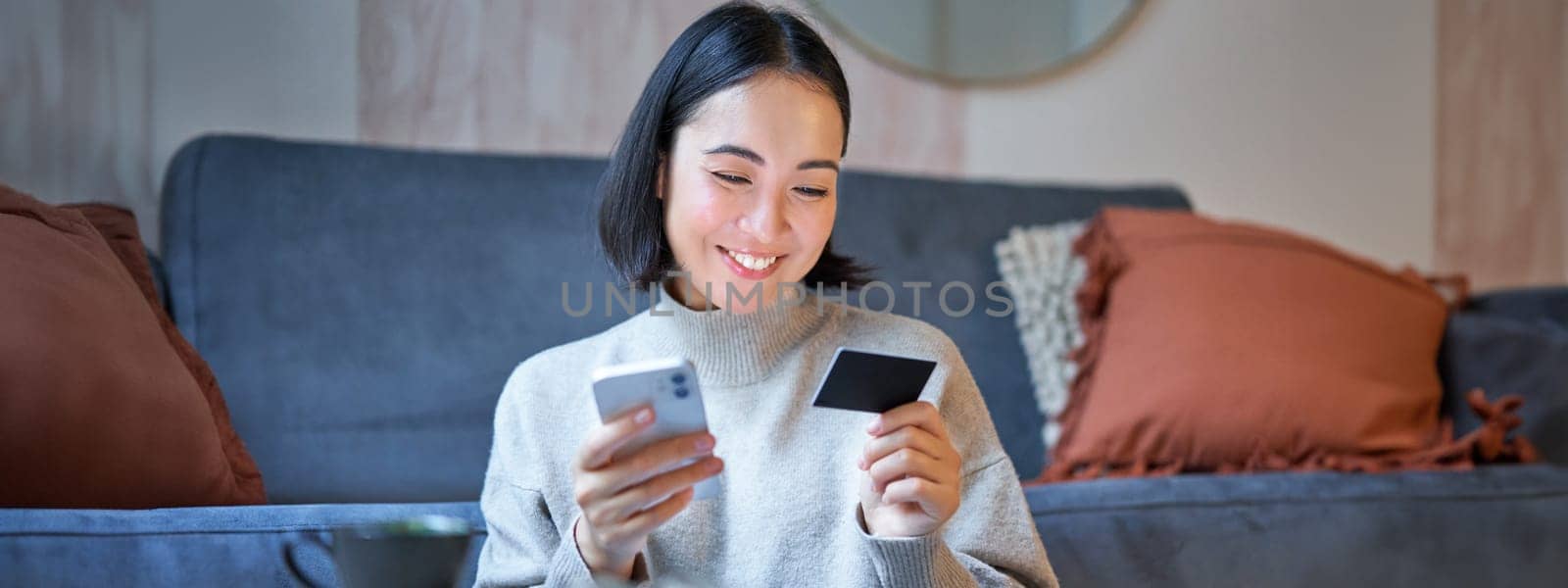 Portrait of smiling asian woman paying with credit card on her smartphone app, arrange direct debit or shopping online from mobile phone.