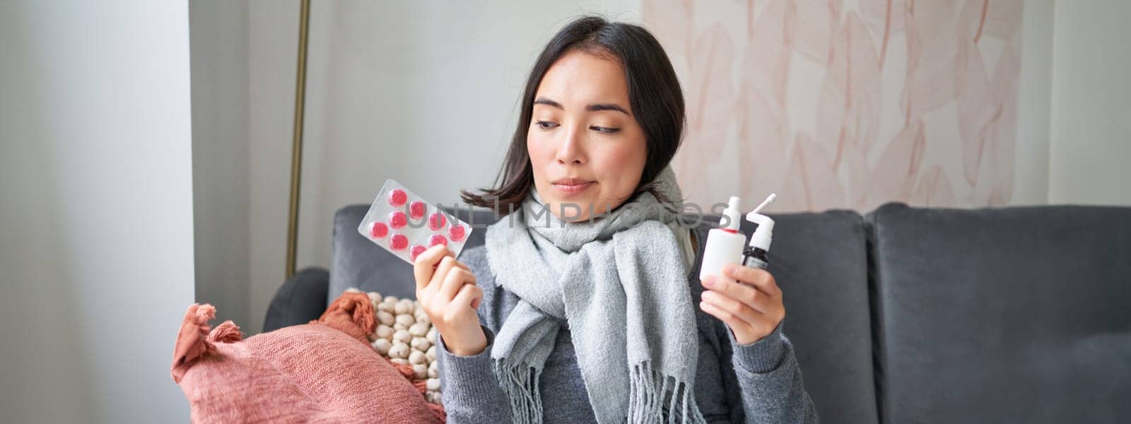 Korean woman showing medical pills, sore throat sprays, feeling sick, staying at home as feeling unwell, catching cold in winter.