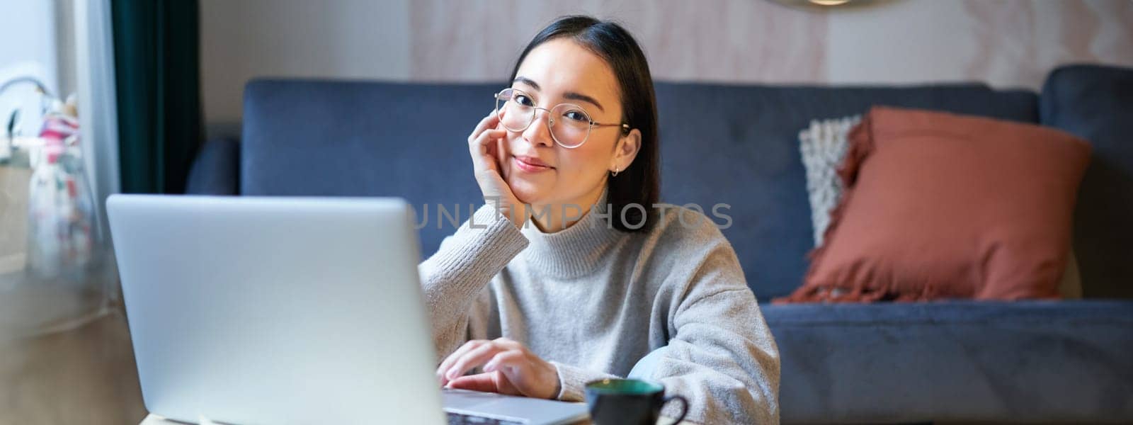 Young asian girl, freelancer professional sitting in living room and working with computer, studying at home using computer.