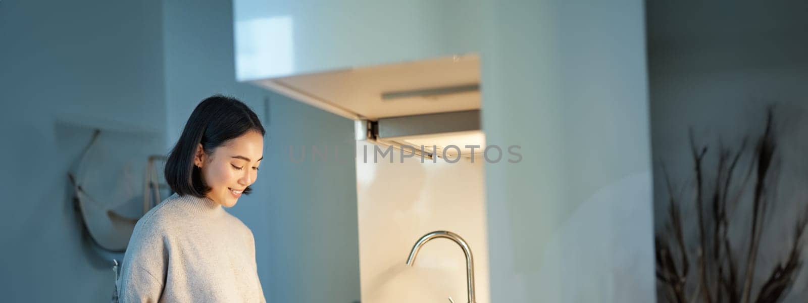Vertical shot of young asian woman cooking dinner, making herself sandwitch, smiling while standing on the kitchen.