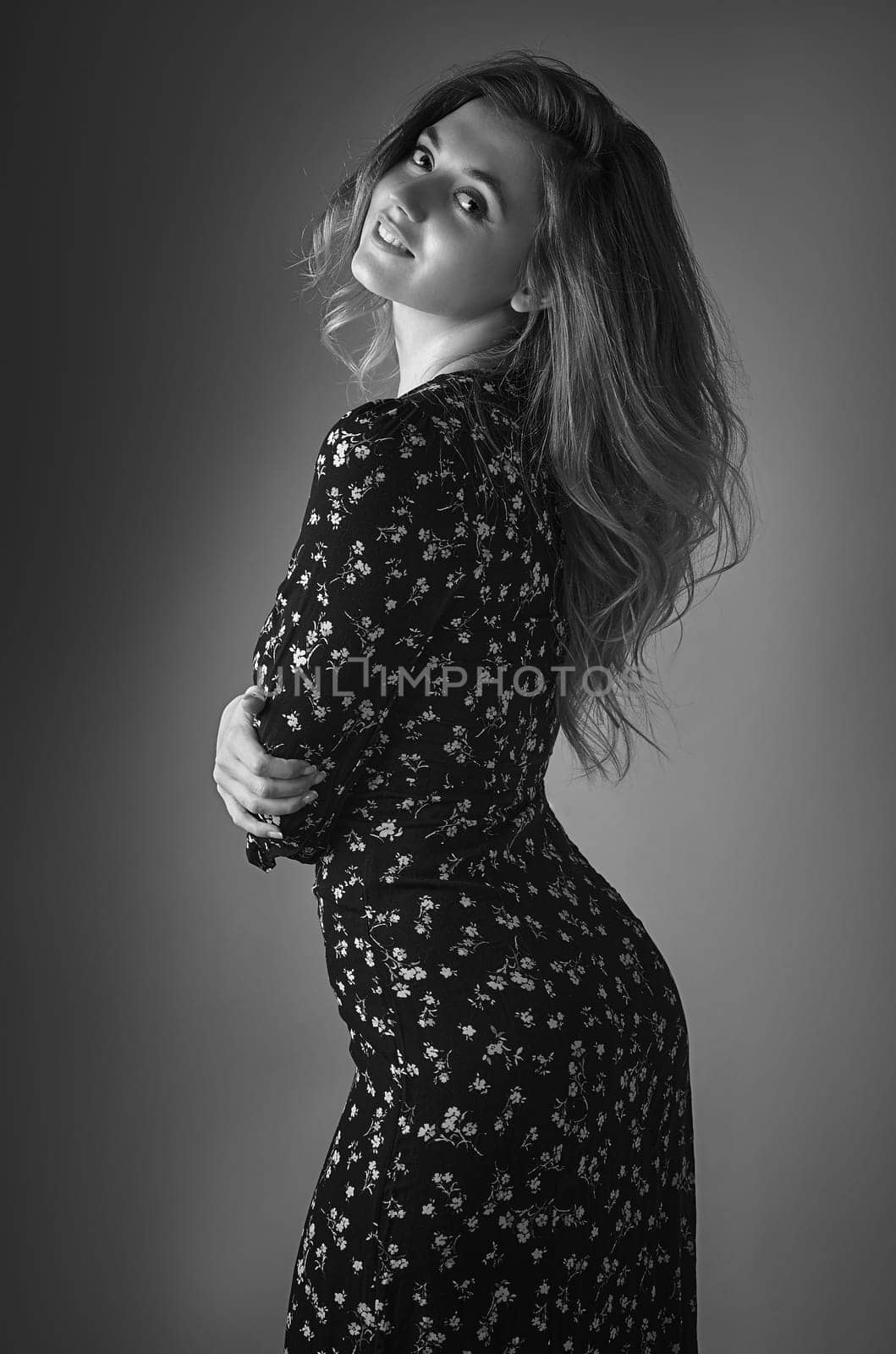 Black and white portrait of a young woman standing sideways and looking at the camera on a dark background