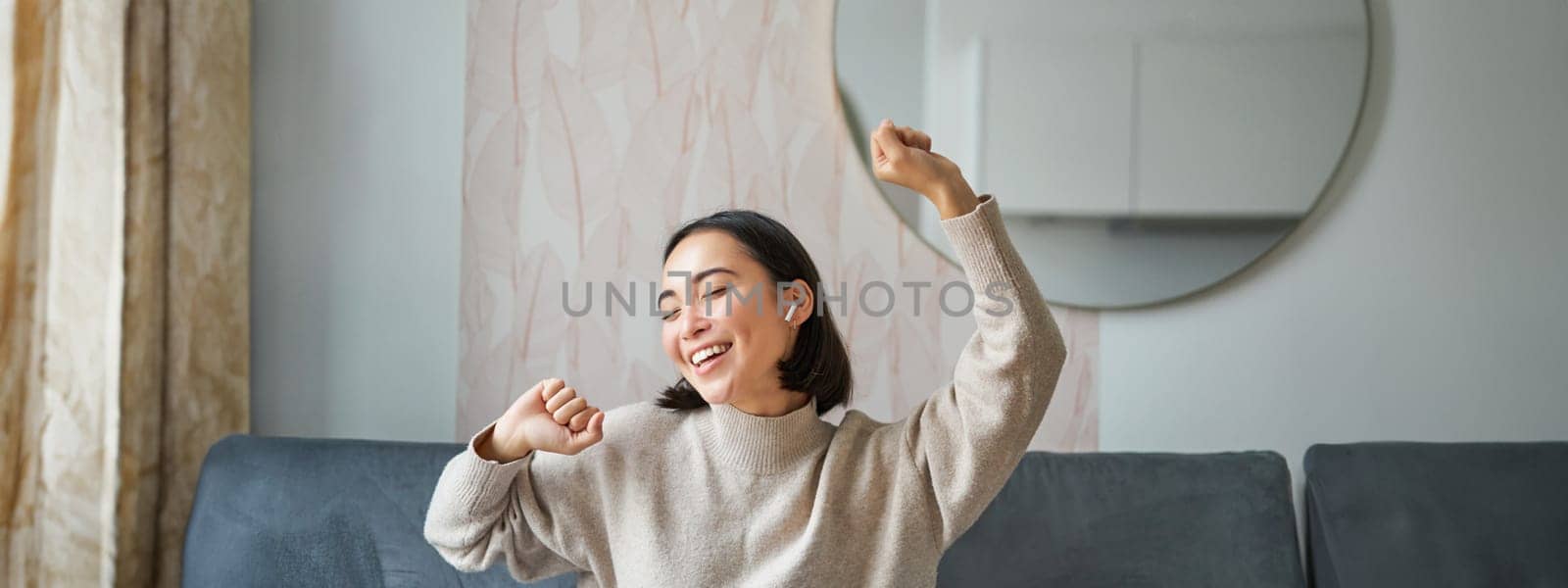 Close up portrait of beautiful asian girl dancing, feeling happy and upbeat, listening music in wireless headphones by Benzoix