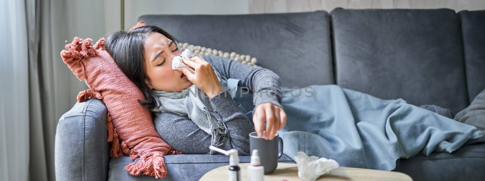 Sick woman lying on sofa at home, catching cold. Young girl freezing from heating problem in her apartment, concept of high cost of living.