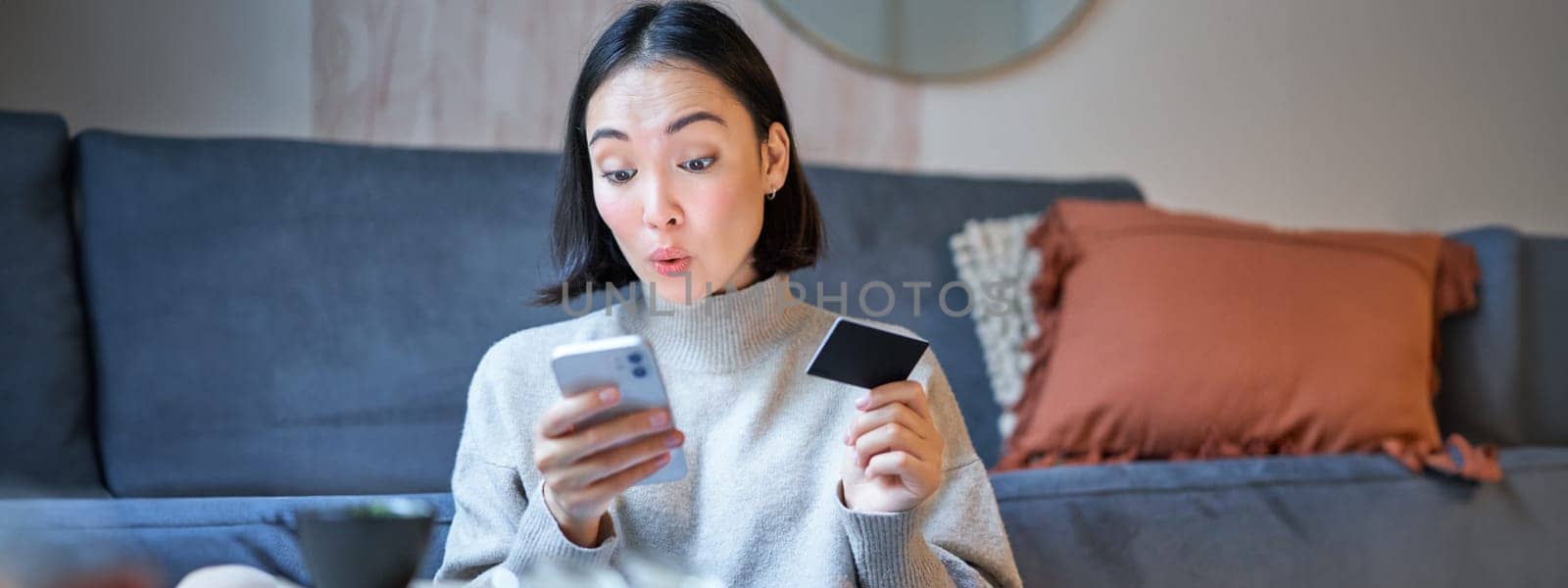 Portrait of smiling korean woman using credit card and smartphone app, paying for purchase, order online delivery.