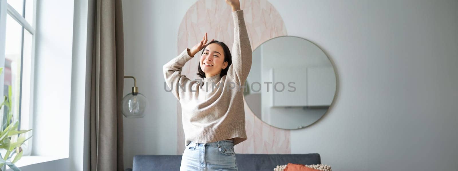 Women and wellbeing. Beautiful young asian woman dancing, feeling carefree and happy, raising her hands above head and smiling, enjoying her stay at home.