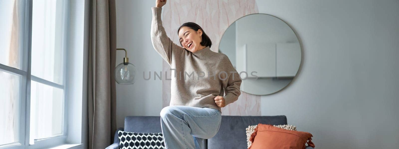 Portrait of happy asian woman dancing, rejoicing and triumphing, feeling upbeat at home. Copy space