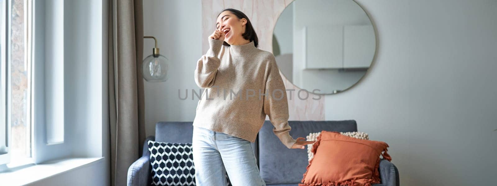 People and emotions. Portrait of asian girl standing in living room, singing in shadow microphone, dancing and having fun, feeling joy.