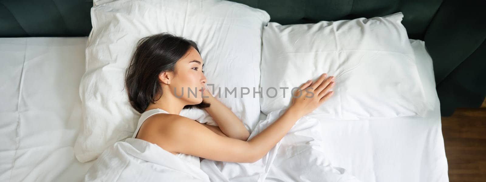 Portrait of romantic asian woman lying alone in her bed, touching empty pillow and thinking about her partner, breakup relatioship by Benzoix