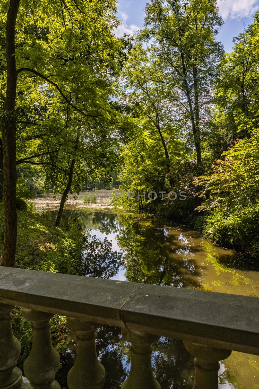 Small stream in beautiful park with colorful surroundings seen from small concrete bridge with beautiful decorations by Wierzchu