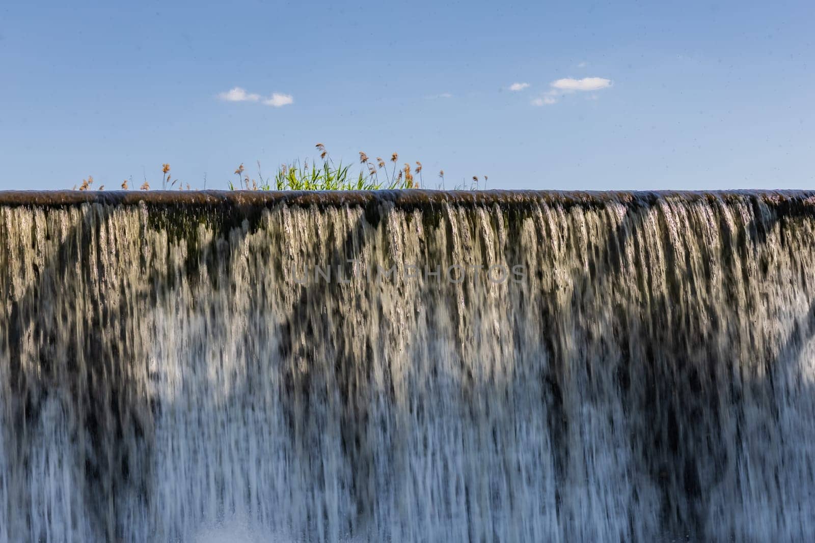 Small waterfall with streaming water over water level at water dam by Wierzchu