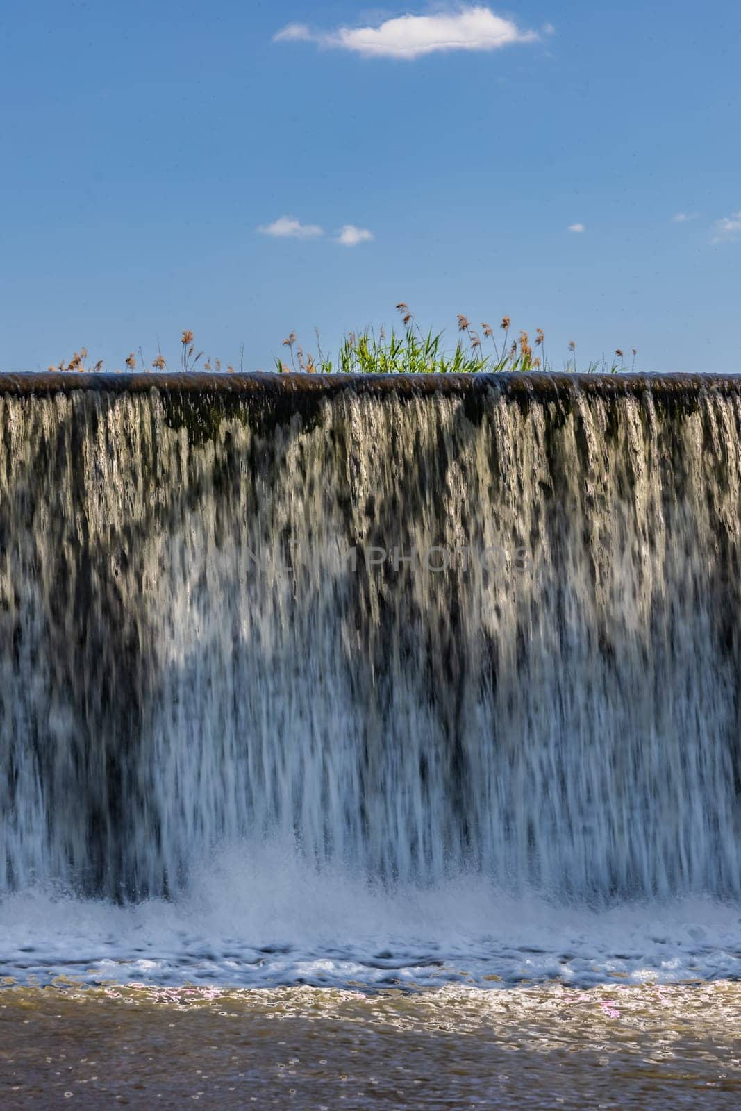 Small waterfall with streaming water over water level at water dam