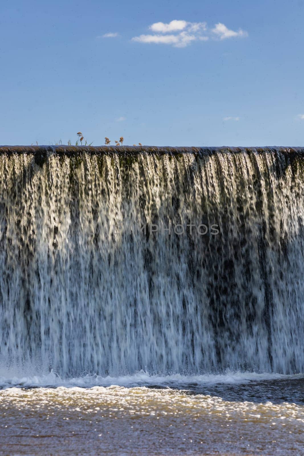 Small waterfall with streaming water over water level at water dam