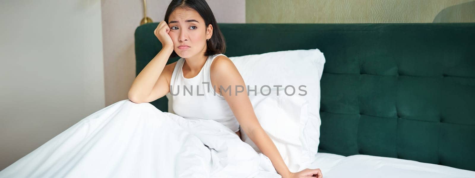 Portrait of distressed asian woman lying in bed, looking complicated and upset, cant understand smth, spending time in bedroom by Benzoix