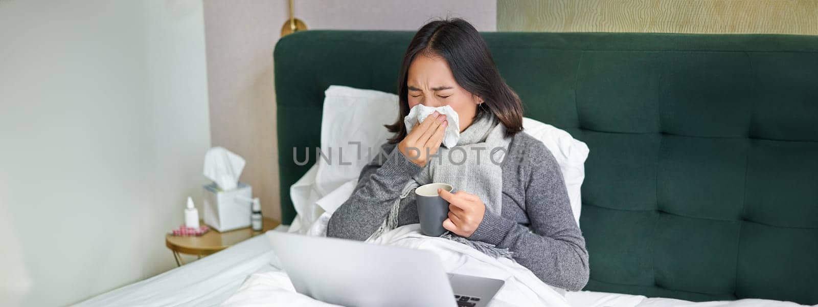 Woman with cold, having flu, staying in bed, sneezing in napkin, runny nose and influenza symptoms by Benzoix