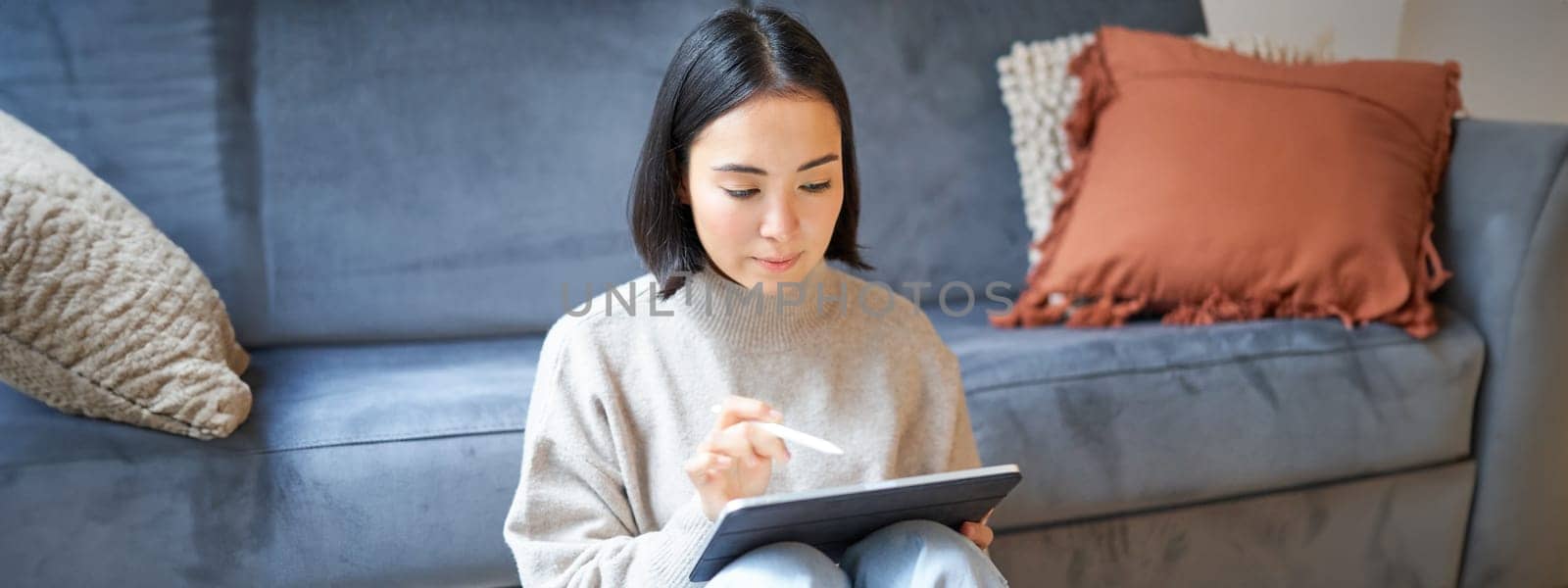 Creative young woman sitting with tablet and pen, drawing on digital application.