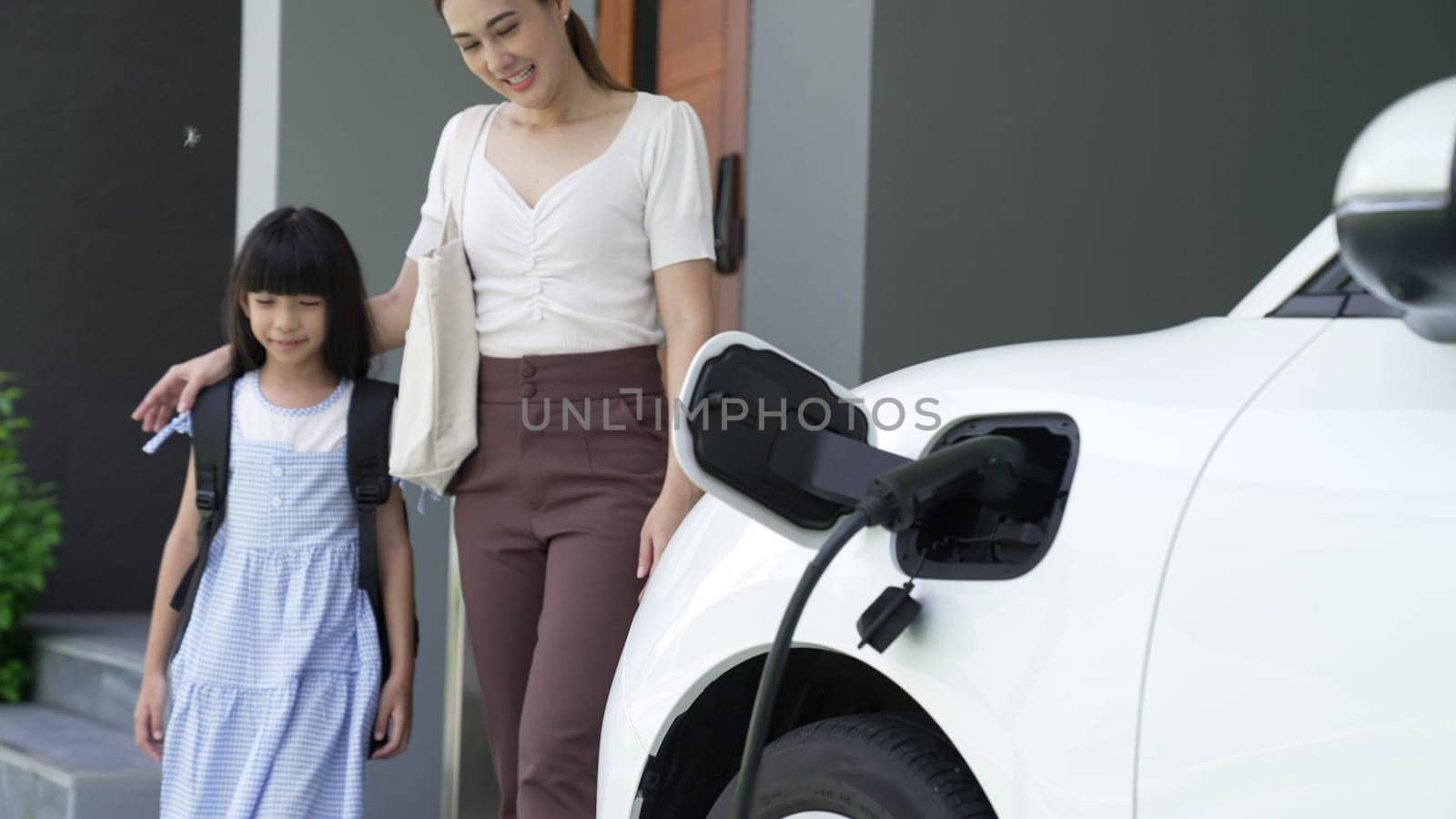 Progressive lifestyle of mother and daughter who have just returned from school in an electric vehicle that is being charged at home. Electric vehicle powered by sustainable clean energy.