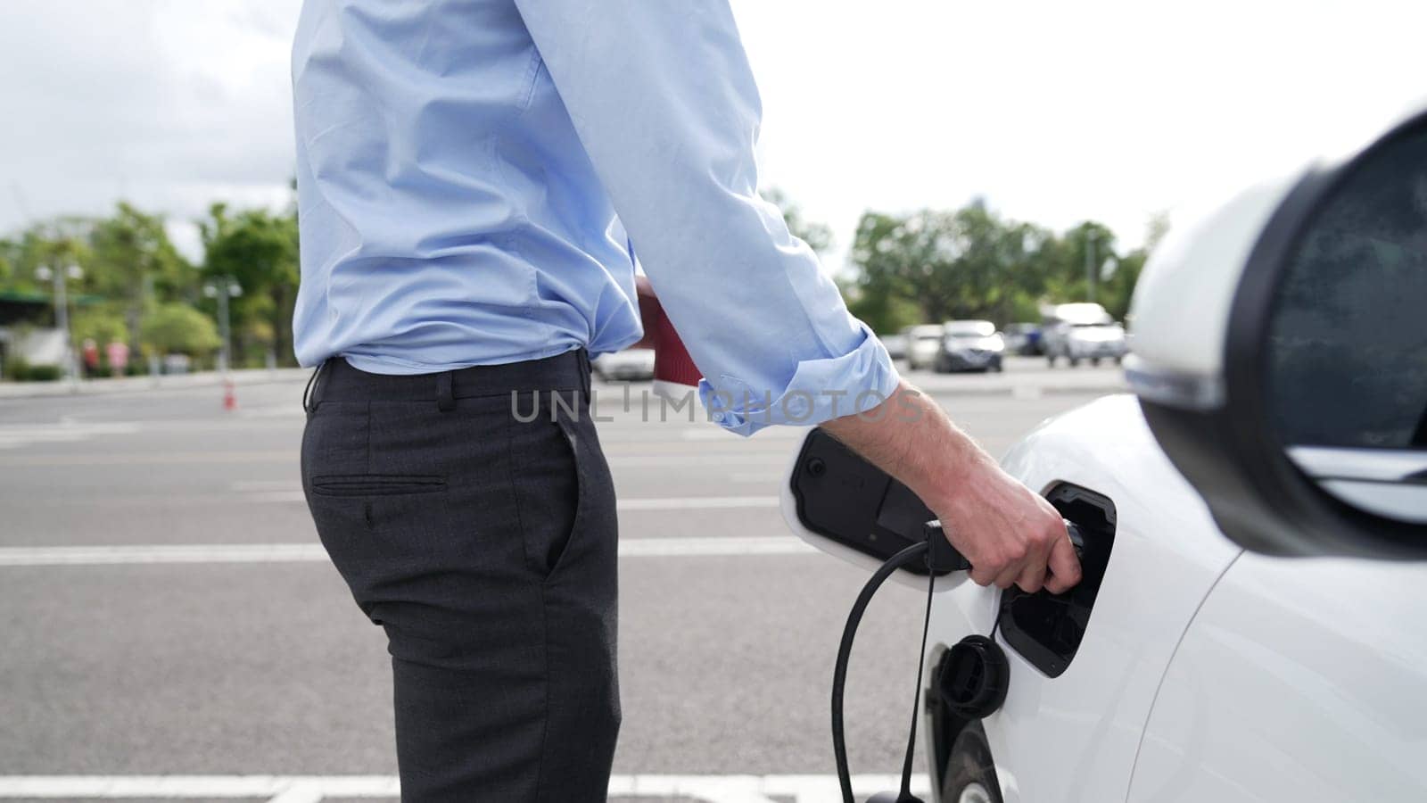 Progressive businessman install charger plug from charging station to his electric car before driving around city center. Eco friendly rechargeable car powered by sustainable and clean energy.