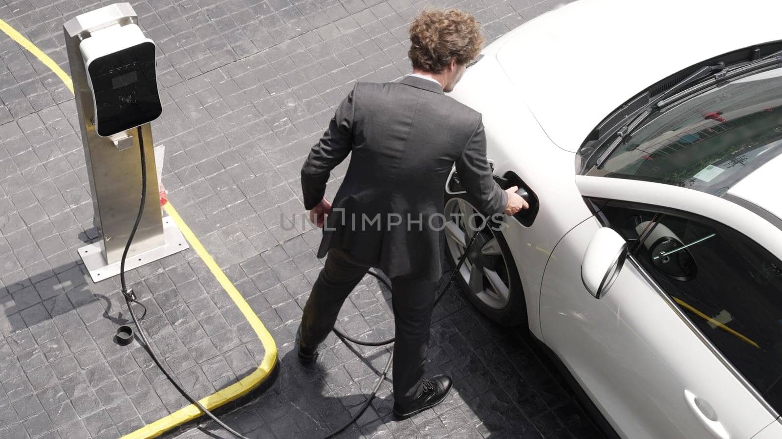 Progressive businessman install charger plug from charging station to his electric car before driving around city center. Eco friendly rechargeable car powered by sustainable and clean energy.
