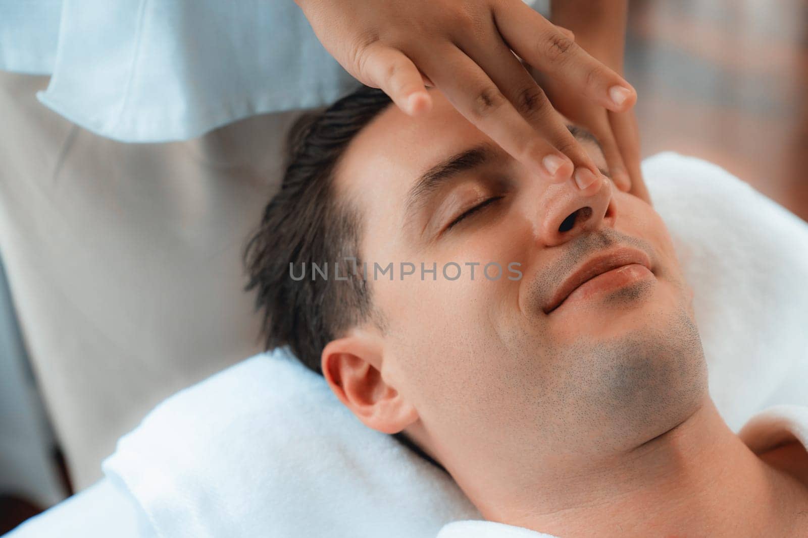 Caucasian man enjoying relaxing anti-stress head massage and pampering facial beauty skin recreation leisure in dayspa modern light ambient at luxury resort or hotel spa salon. Quiescent