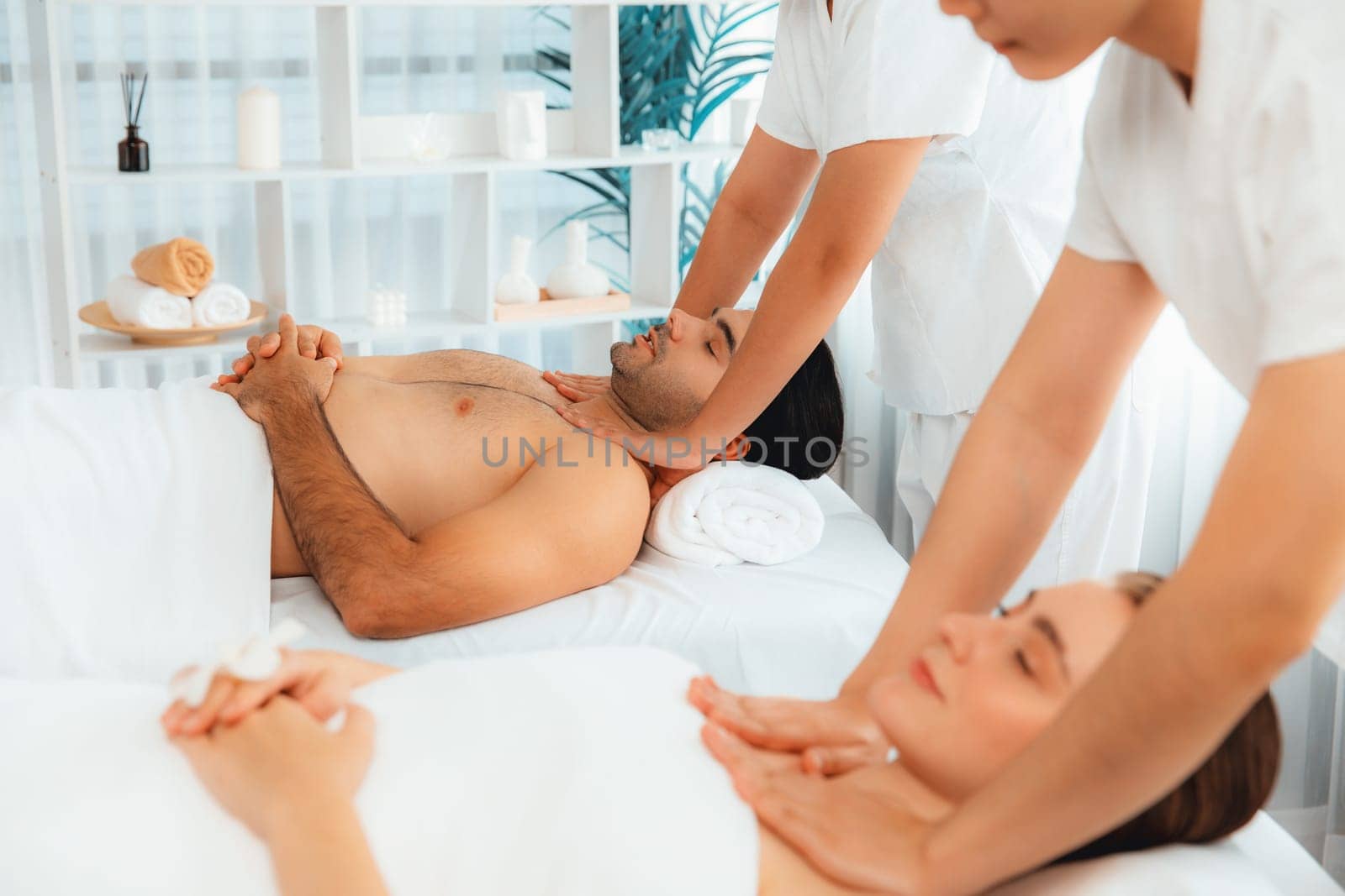 Caucasian couple customer enjoying relaxing anti-stress spa massage and pampering with beauty skin recreation leisure in day light ambient salon spa at luxury resort or hotel. Quiescent