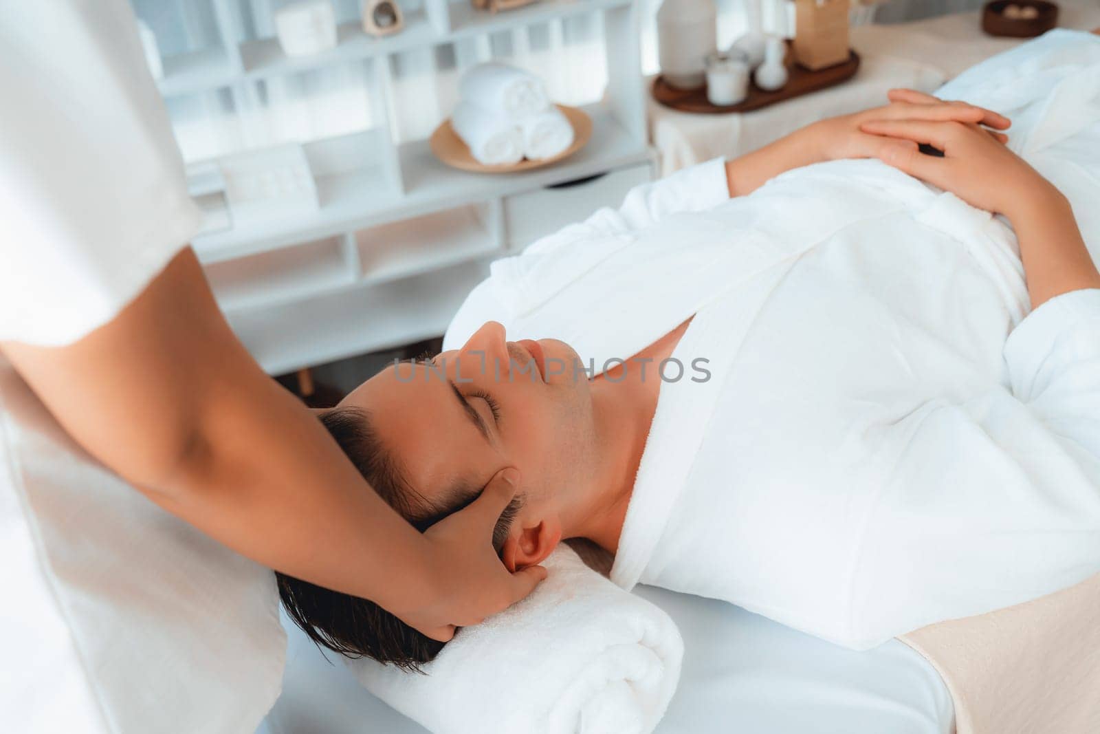 Caucasian man enjoying relaxing anti-stress head massage and pampering facial beauty skin recreation leisure in dayspa modern light ambient at luxury resort or hotel spa salon. Quiescent